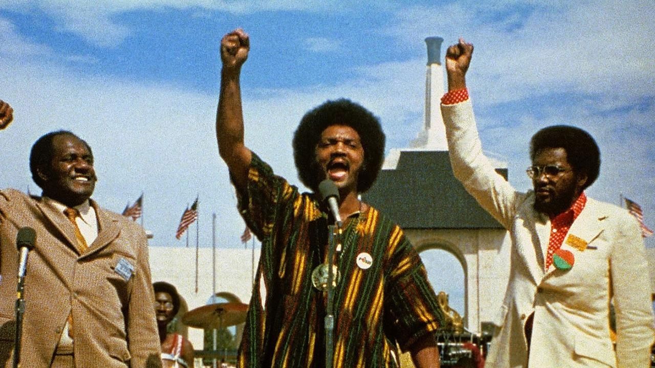 3 men in front of microphones with raised fists